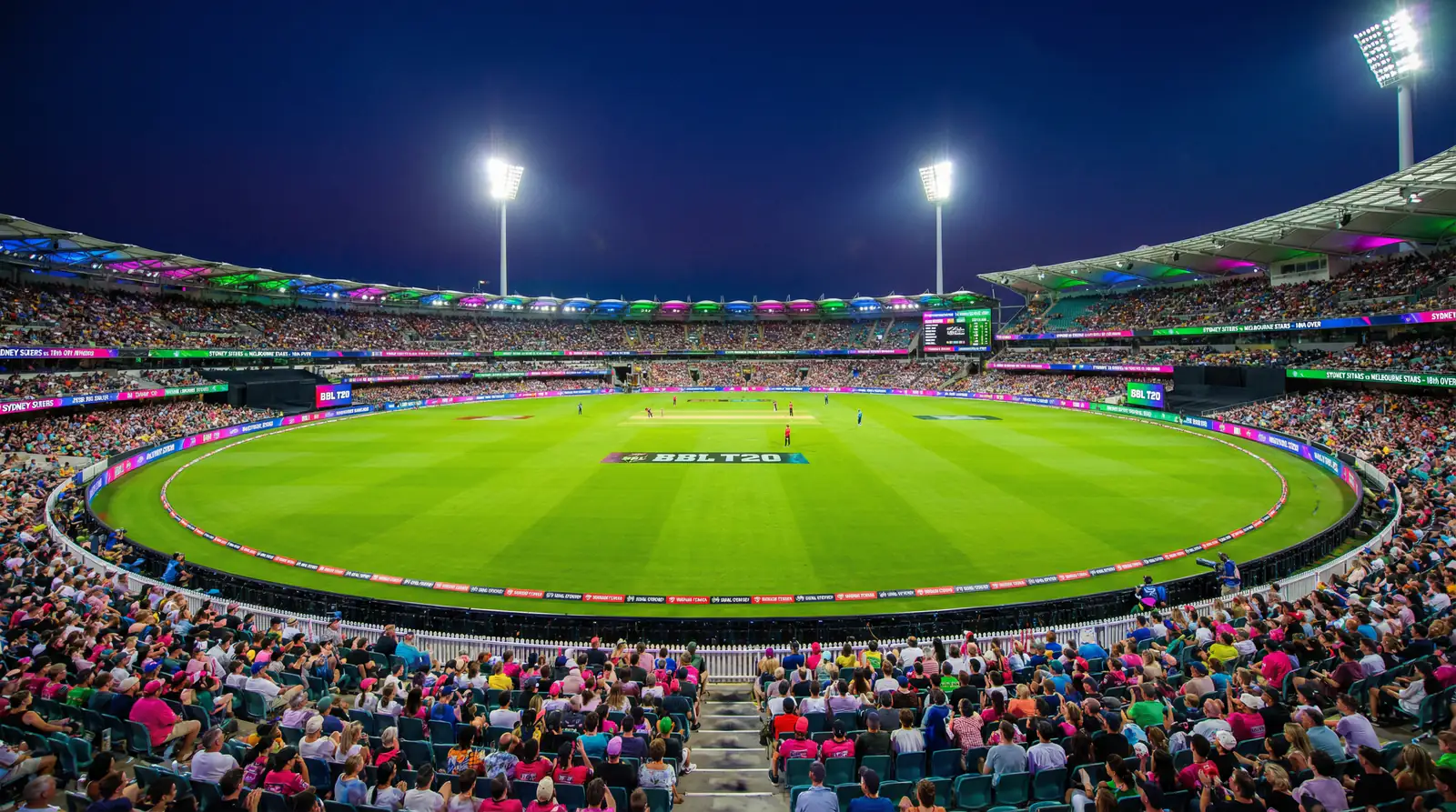 Wide-angle evening view of an Australian cricket stadium during a Big Bash T20 match under colourful floodlights